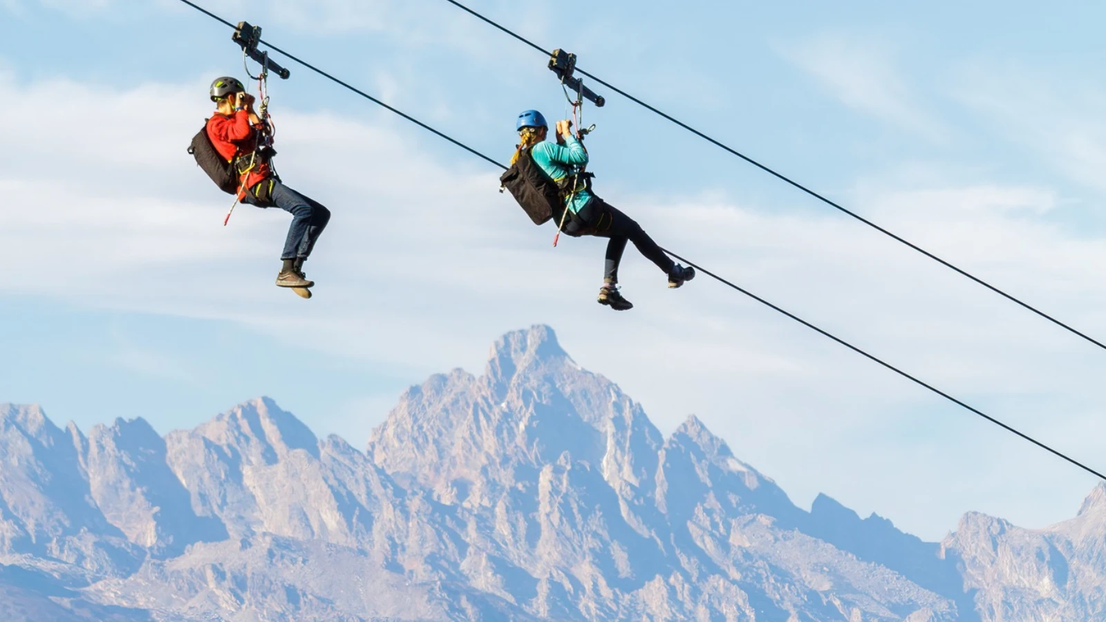 Two people ride the zip line at Snow King Mountain with views of the Grand Teton range in Jackson Hole, WY.