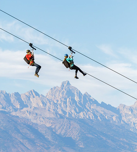 Two people ride the zip line at Snow King Mountain with views of the Grand Teton range in Jackson Hole, WY.