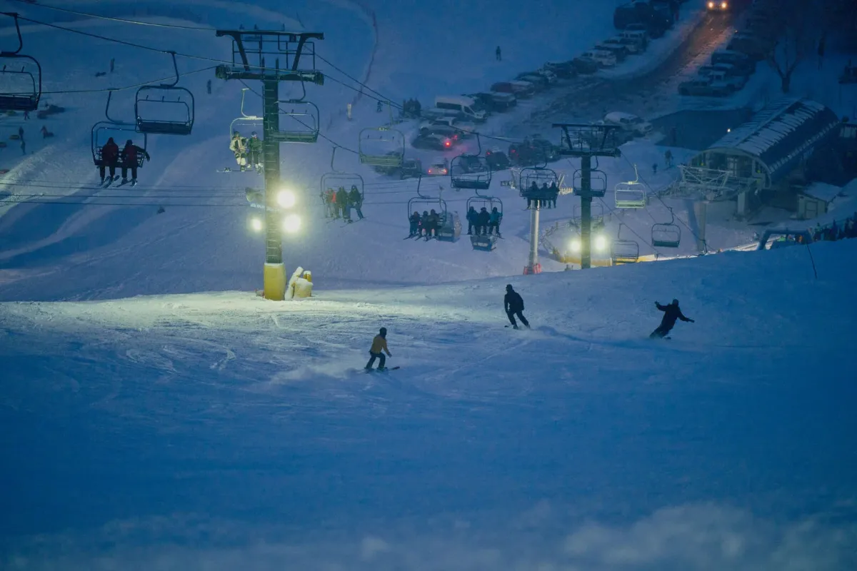 Skiers and snowboarders riding a lit slope under the chairlift during night skiing at Snow King Mountain in Jackson, Wyoming