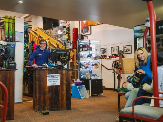 Staff member at the counter of the Snow King Mountain winter rental shop with skis, snowboards and boots on display behind him